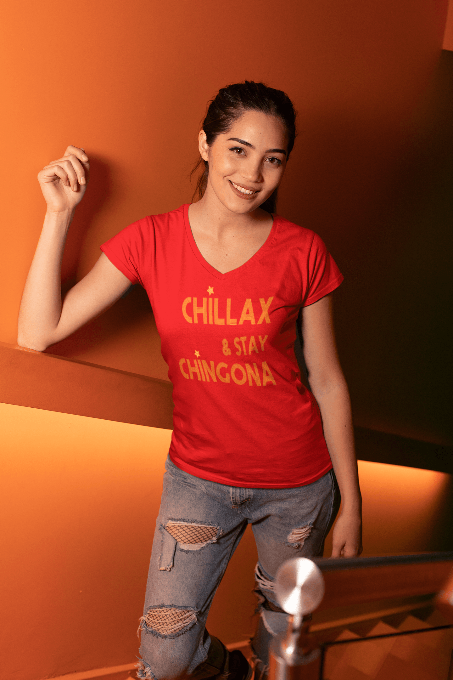 Red V-neck t-shirt with the text, "Chillax Y Stay Chingona" in streetwear font and yellow ink. This sexy tee comes in sizes small thru 3XL. It is available at www.sanchezhere.com