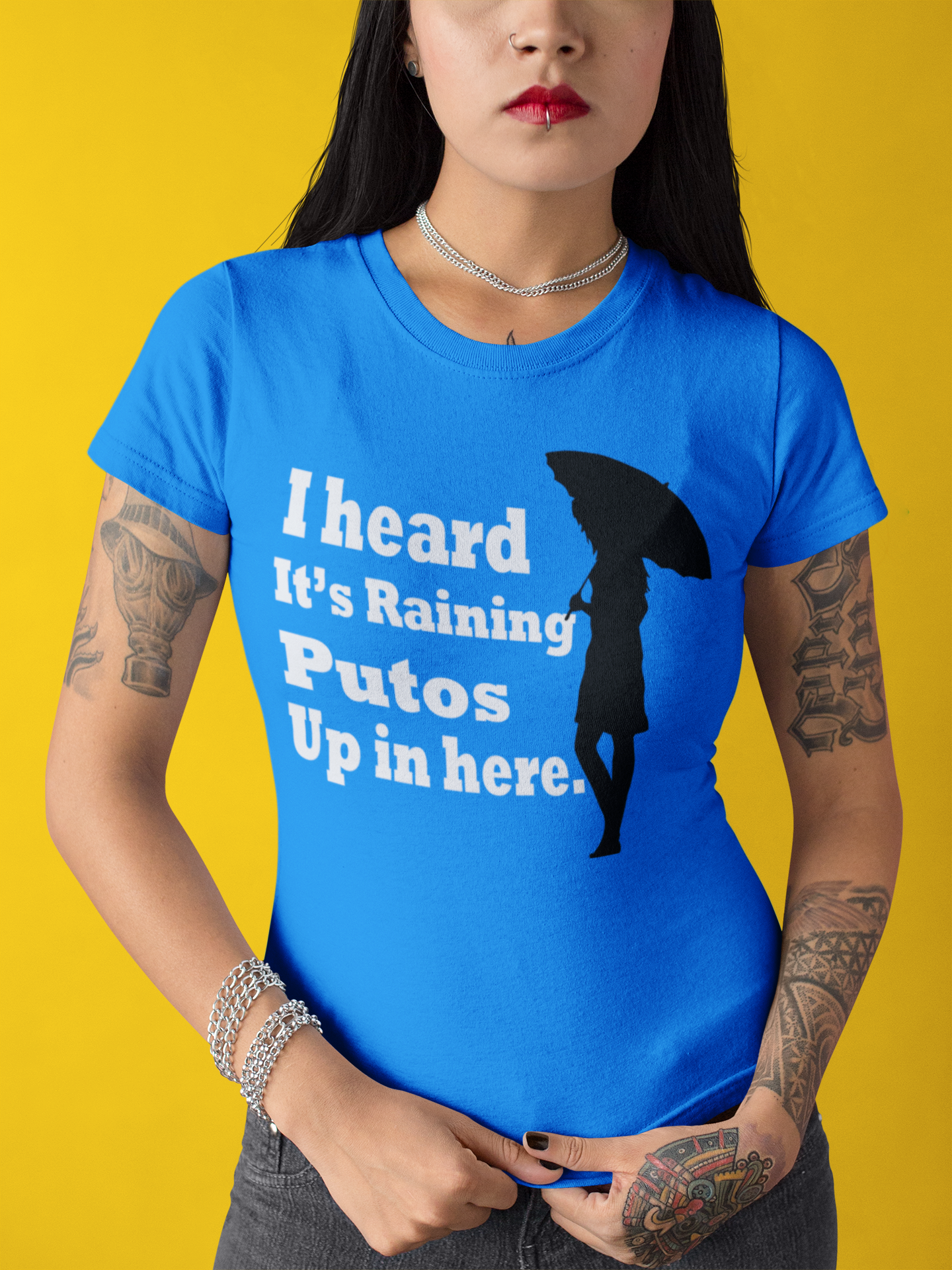Blue T-shirt with the text, "I heard it's raining putos up in here" in white ink and a shadow woman holding an umbrella in black. This sassy tee comes in sizes small thru 4XL. It is available at www.sanchezhere.com