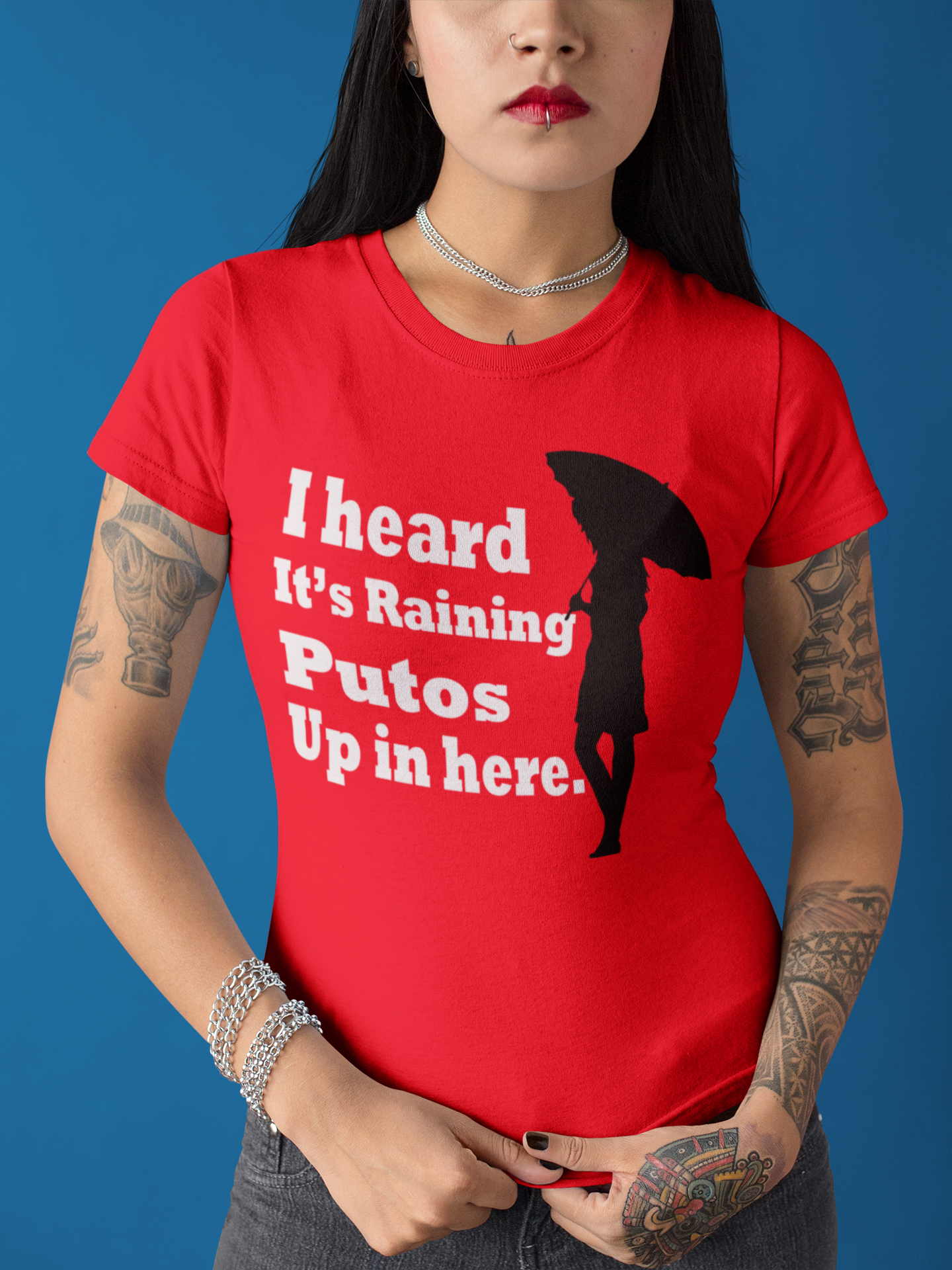 Red T-shirt with the text, "I heard it's raining putos up in here" in white ink and a shadow woman holding an umbrella in black. This sassy tee comes in sizes small thru 4XL. It is available at www.sanchezhere.com