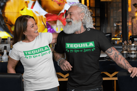 Picture of man and woman wearing Black and White  Unisex T-shirts with the text, Tequila My Kind of shots, and a picture of two shot glasses in lime green ink. This tee comes in sizes small-3xl and is available at www.sanchezhere.com
